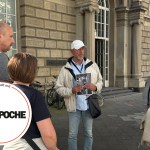 Eine Gruppe von Menschen steht vor einem großen Gebäude in der Düsseldorfer Altstadt. Einer hält ein Foto in der Hand und unterhält sich angeregt. Vielleicht sind sie Teil einer „Historischen Tour“, bei der wir die reiche Vielfalt der Stadtvergangenheit erkunden.