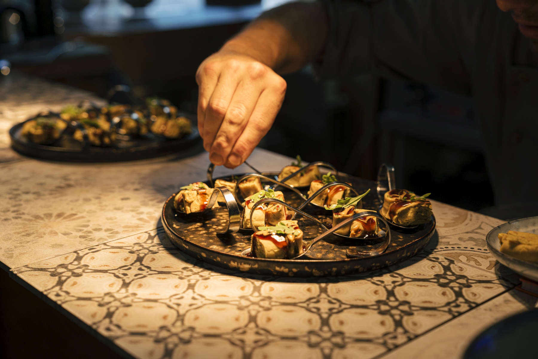 Der Küchenchef garniert kleine, kunstvoll angerichtete Vorspeisen auf einer dekorativen Platte, perfekt für ein elegantes Dinner-Hopping-Erlebnis in Frankfurt.