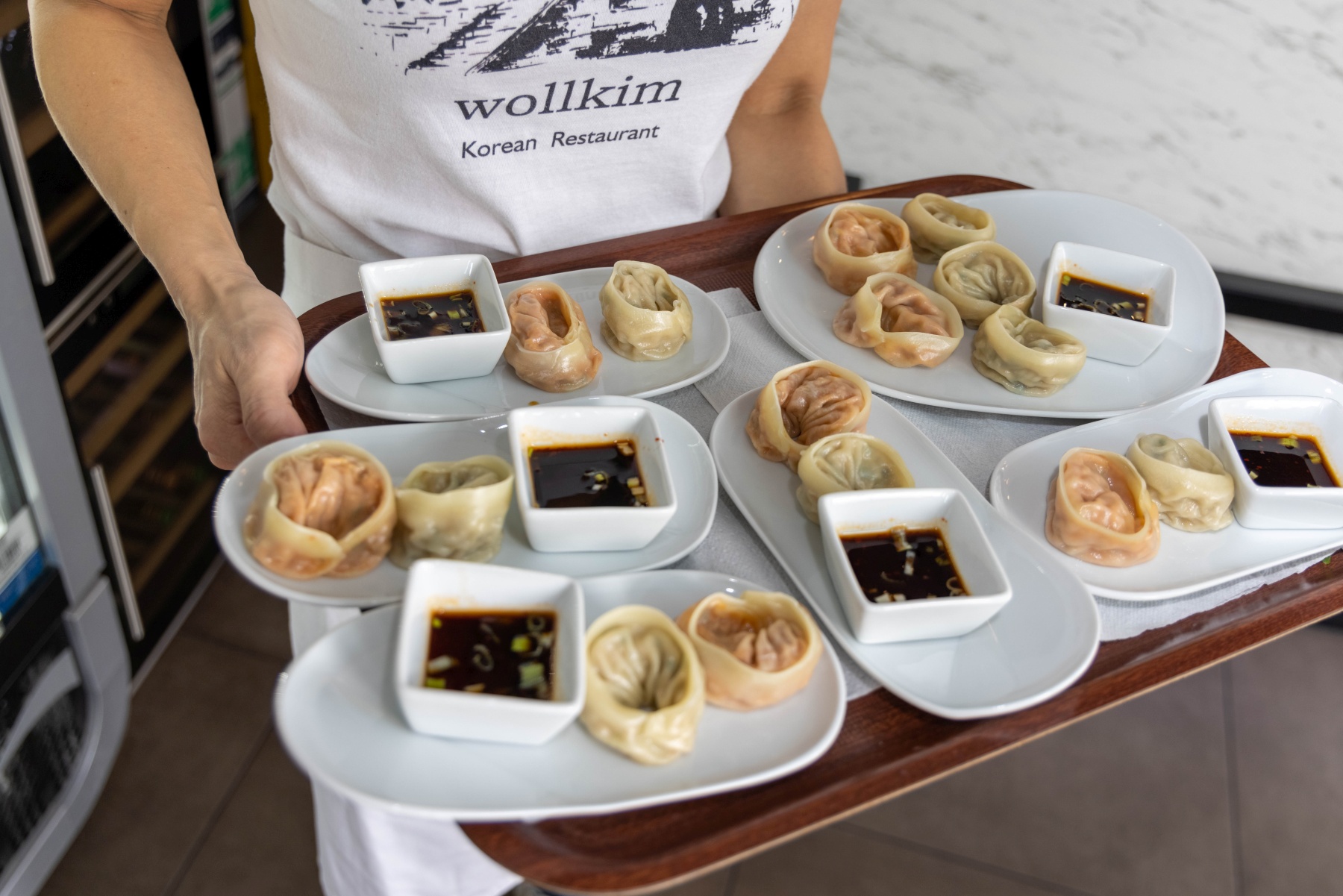 In einem belebten koreanischen Restaurant in Frankfurt balanciert eine Person gekonnt ein Tablett voller Teigtaschen und pikanter Dip-Sauce und verkörpert so den Geist des Dinner-Hoppings durch kulinarische Genüsse.