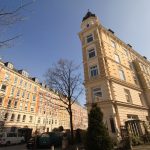 Straßenansicht eleganter, mehrstöckiger Wohnhäuser in Hamburg Ottensen mit Bäumen und in der Sonne geparkten Autos.